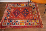 Vintage Turkish rug corner, geometric border in indigo, orange, yellow, red, and frayed fringe.