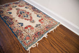 Fringed corner of a vintage 1940s Kerman rug with rose and indigo floral motifs.