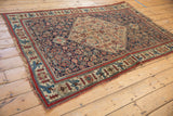 Antique Bijar rug corner showcasing detailed red and blue floral, bird motifs on a dark indigo field.