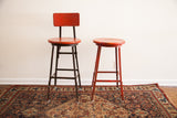 Pair of vintage 1940s industrial machinists stools, one with back, chippy red paint.