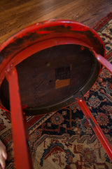 Vintage industrial stool underside, showing chippy red paint, metal frame, and dark wood base.