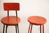 Distressed chippy red paint on a vintage industrial stool pair, one with back, one without.