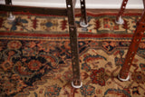 Industrial metal stool legs, one dark and one chippy red, standing on a traditional rug.