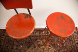 Chippy red paint texture on the round seats of two vintage industrial stools.
