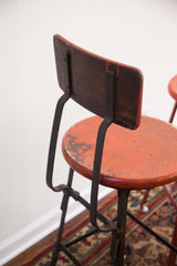 Close-up of the vintage industrial stool's chipped red seat and dark wood back.