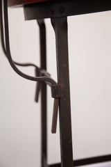 Industrial metal stool detail showing dark frame, adjustment pin, and aged texture.