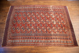 Vintage Bokhara rug showing repeating guls in rust red and navy, with isolated wear.