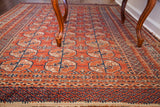 Vintage Bokhara rug displaying repeating red-orange and navy geometric gul motifs.