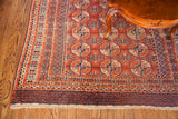 Vintage Bokhara rug corner, terracotta geometric guls, dark blue borders, and fringe.