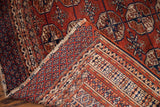Vintage Tekke Bokhara rug folded, revealing woven back, fringe, and geometric gul design.