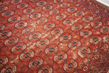 Rhythmic brick red field and navy Bokhara motifs of the antique Tekke rug, with authentic wear.