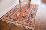 Close-up of vintage pink-orange Turkish rug: geometric double tree design, blue borders, fringe.