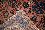 Vintage Persian rug corner revealing exposed foundation and wear, with detailed rose and indigo patterns.