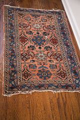 Corner of vintage Persian Hamadan rug, showing end loss, exposed foundation, and indigo border with snail shell motif.