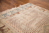 Aged ivory field of an antique Turkish rug, displaying burgundy repeating motifs and blue geometric border with fringe.