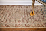 Aged ivory 18th century Turkish rug with repeating motif, muted burgundy, teal accents, and faux fringe.