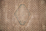 Aged ivory antique Turkish rug detail: faded teal diamond medallion and burgundy repeating motifs.