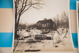 Vintage 1940s photograph of a house and a classic car in a snowy, wooded landscape.