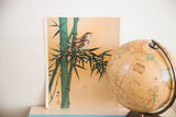 Vintage Asian art lithograph of two birds perched on green bamboo stalks against a warm tan background.
