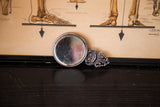 Ornate filigree metalwork and slight scratches on the vintage handheld mirror's reverse.