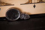 Vintage handheld mirror's ornate metal reverse, featuring fine scrollwork and visible glass wear.