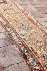 Detailed view of antique Northwest Persian rug's geometric patterns, teal, madder red, and worn edge.