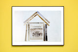 Black-framed print of the antique photograph house collage hung on a vibrant yellow wall.
