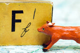Textured miniature orange fox with green eyes beside a vintage yellow book with the letter F.