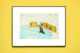 T is for T-Rex art print with a miniature dinosaur and alphabet books on a vintage map of Italy.
