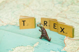 Vintage alphabet blocks spelling T REX behind a miniature dinosaur on a vintage Italian map.
