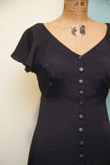 Black Betsey Johnson dress with V-neck, flutter sleeves, and central buttons.
