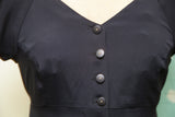 Betsey Johnson black dress featuring five dark buttons with light dot centers.