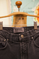 Versace Jeans Couture label and gold Medusa head button on faded black denim.