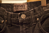 Detail of Versace Jeans Couture faded black denim waistband, Medusa button, and logo tag.