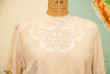Dainty embroidered applique detailing the neckline of the vintage ivory silk blouse.