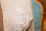 Ivory cashmere sweater with intricate white beaded floral motifs and pearl button.