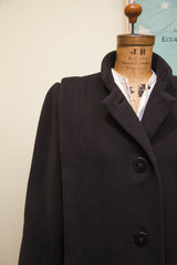 Trigere black coat with sculpted 40s shoulder and textured wool fabric.