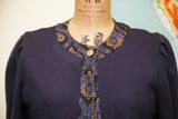 Navy blue knit sweater's ornate trim featuring blues, gold, purple, with a single button.