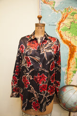 Moschino buttondown blouse features vibrant red flowers and white designer script.