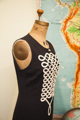 Side profile of a vintage Moschino black dress with intricate white piping detail.