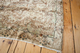 Vintage Kerman rug corner with low pile, worn fringe, and muted baroque rococo patterns.