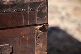 Close-up of the riveted corner and aged, cracked metal hardware on the wooden trunk.