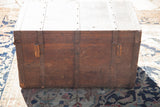 Front of an antique wooden trunk with a rich red patina and dark metal strapping.