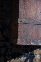 Weathered dovetail corner and riveted metal banding on an antique hardwood trunk.