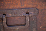 Weathered iron handle and riveted metal strapping on the antique wooden trunk.