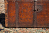 Close view of the antique trunk's iron latch, skeleton keyhole, and red patina wood grain.