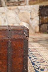 Cracked corner joint and riveted metal strap on an antique wooden trunk with deep patina.