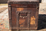 Side view of an antique wooden trunk with its rustic metal handle and riveted straps.