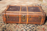 Vintage Indestructo trunk with bent wood, metal corners, and aged brass patina.