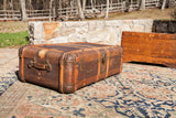 Vintage Indestructo trunk coffee table with rusty orange patina, bent wood, and metal corners.